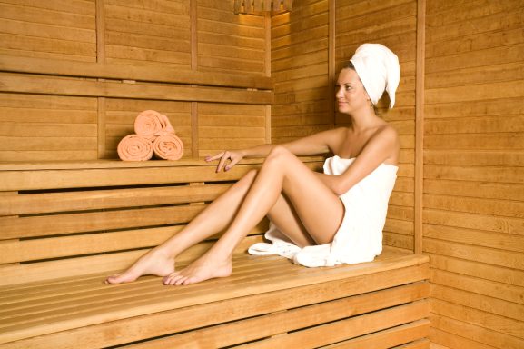 Frau in einer Sauna, sitzend auf einer Holzbank, mit Handtuch und Lächeln.