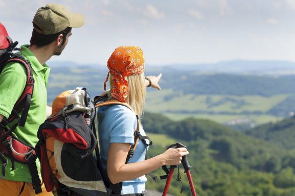 Ein Mann und eine Frau mit Rucksäcken blicken auf eine hügelige Landschaft.