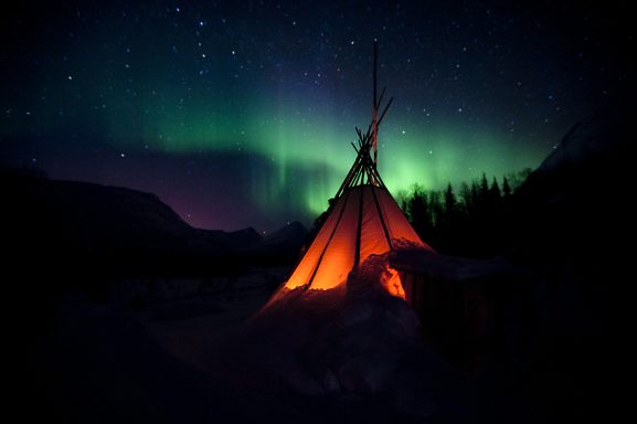 Zelt unter dem Sternenhimmel mit farbenprächtigen Nordlichtern.