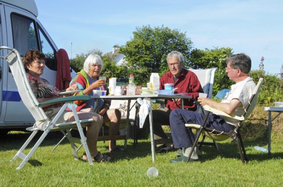 Vier Personen sitzen an einem Tisch im Freien und genießen ein Picknick. Sunny day.