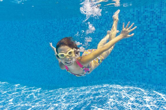 Ein fröhliches Kind taucht unter Wasser mit einer Schwimmbrille und buntem Badeanzug.