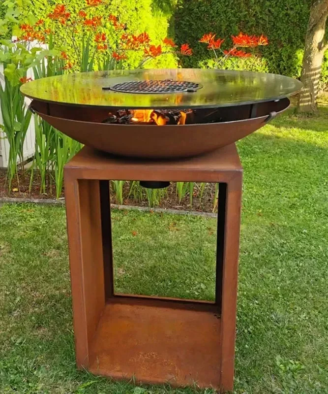 Feuerstelle aus Metall auf einem quadratischen, rostfarbenen Tisch im Garten.