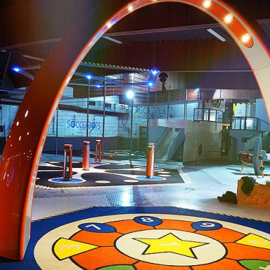 Spielplatz mit bunten Böden und verschiedenen Spielelementen in einem Indoor-Bereich.