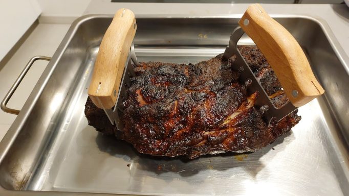 Gegrilltes Fleischstück mit Holzgriffen auf einer Metallschale.