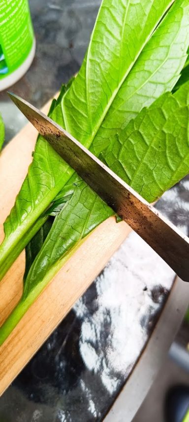 Grüne Blätter werden mit einer Schere auf einem Holztisch geschnitten.