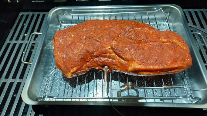 Rohes gewürztes Fleischstück auf einem Grillrost in einer Auffangschale.