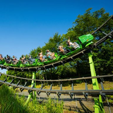 Achterbahn mit Fahrgästen, die eine Kurve in einem Freizeitpark fahren.