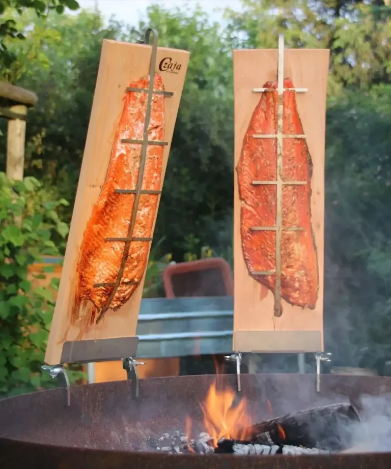 Zwei durch Holzbretter gesicherte Fischfilets über offenem Feuer grillend.