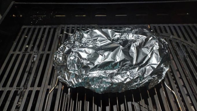 Ein Stück Alufolie liegt auf einem Grillrost.