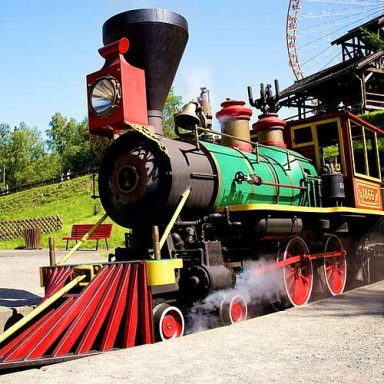Bunte Dampflokomotive mit großem Schornstein und Detailarbeiten, auf Schienen stehend.