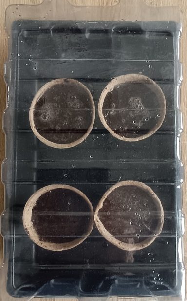Zwei runde, braune Behälter auf schwarzer Plastikverpackung.